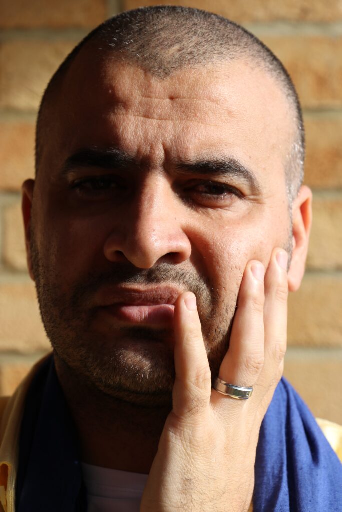 A photograph of Yousif M. Qasmiyeh with his left hand on his left cheek.